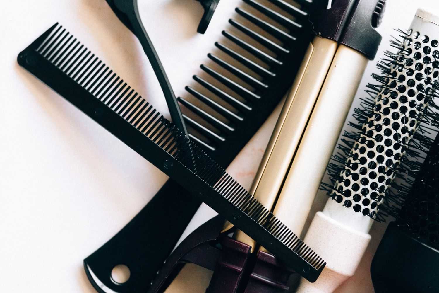 Assorted hair styling tools including combs, curling iron, and brushes against a white background.